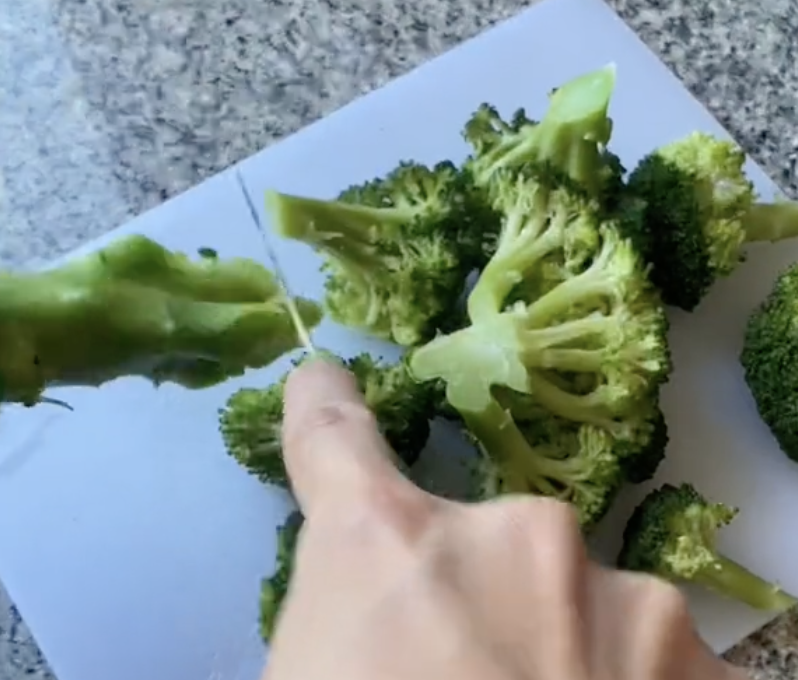 hand cutting off broccoli stem on a chopping board